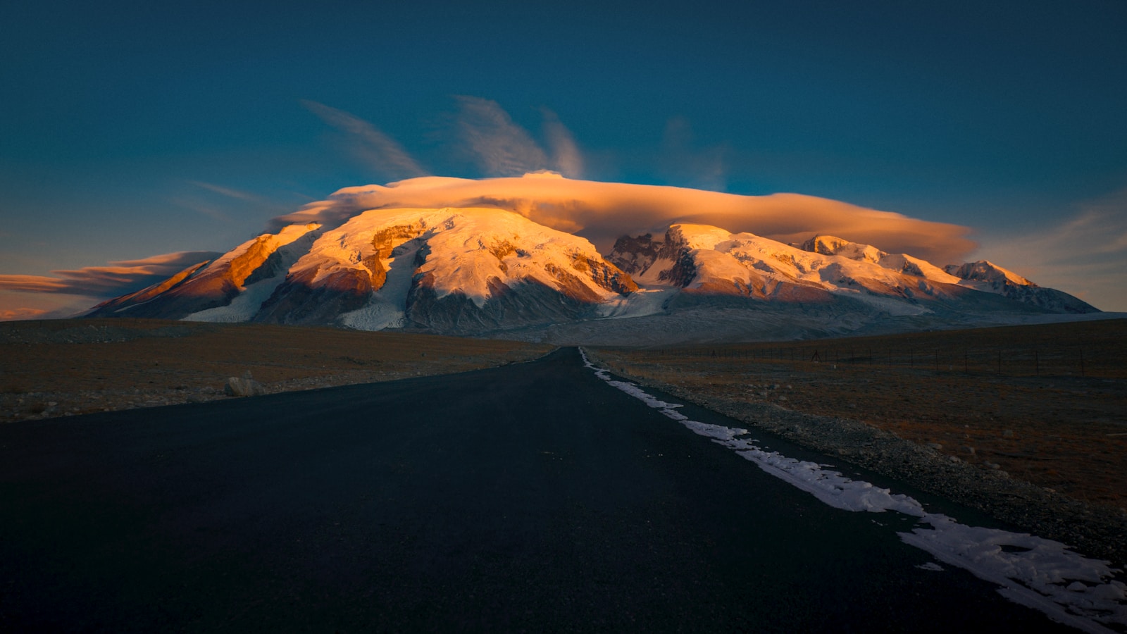 Snow-capped mountain illuminated by sunset with road.