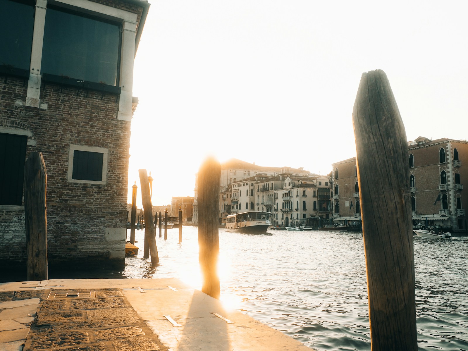 Sunlight glints off a canal with buildings and boat.