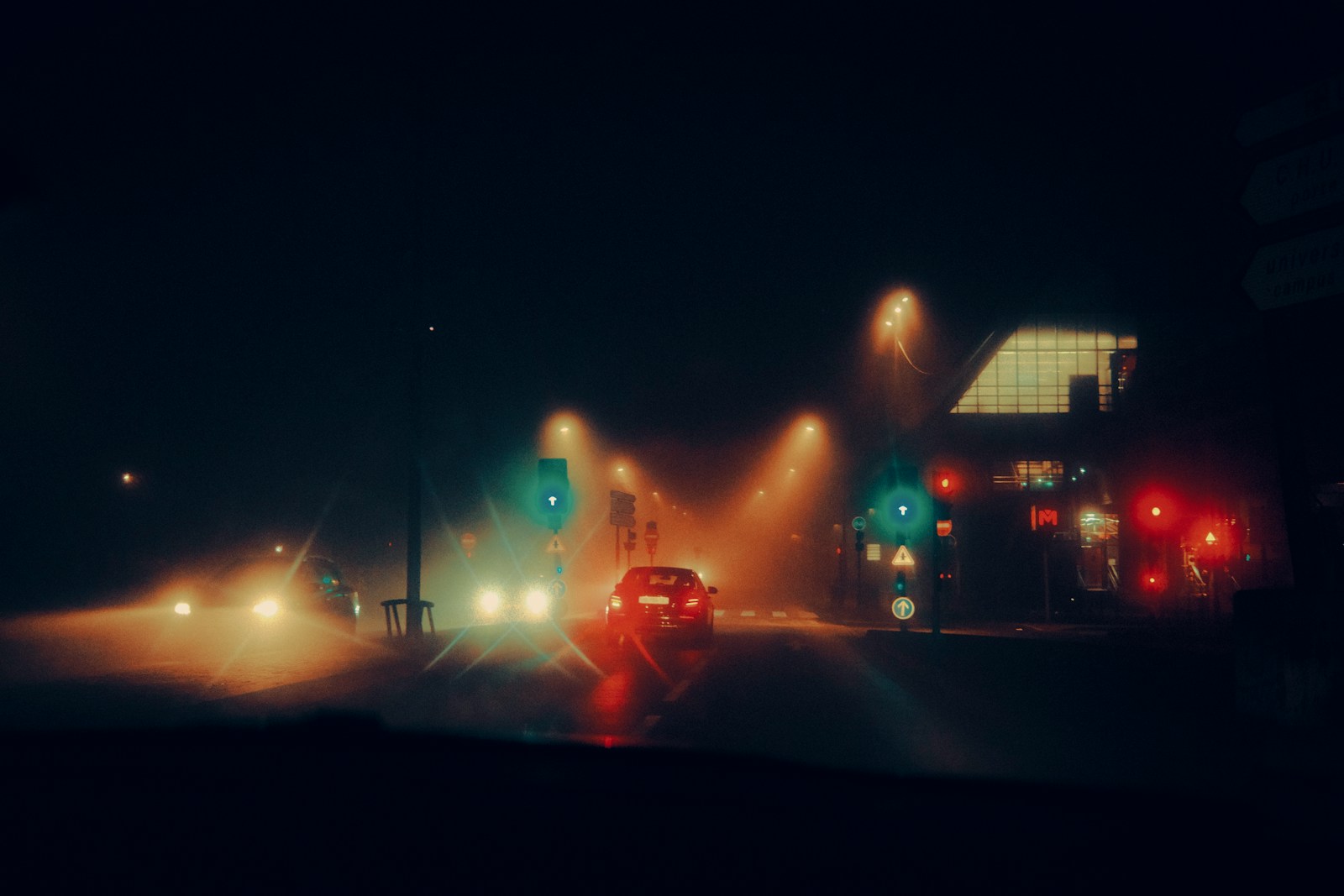 Cars driving on a foggy road at night.