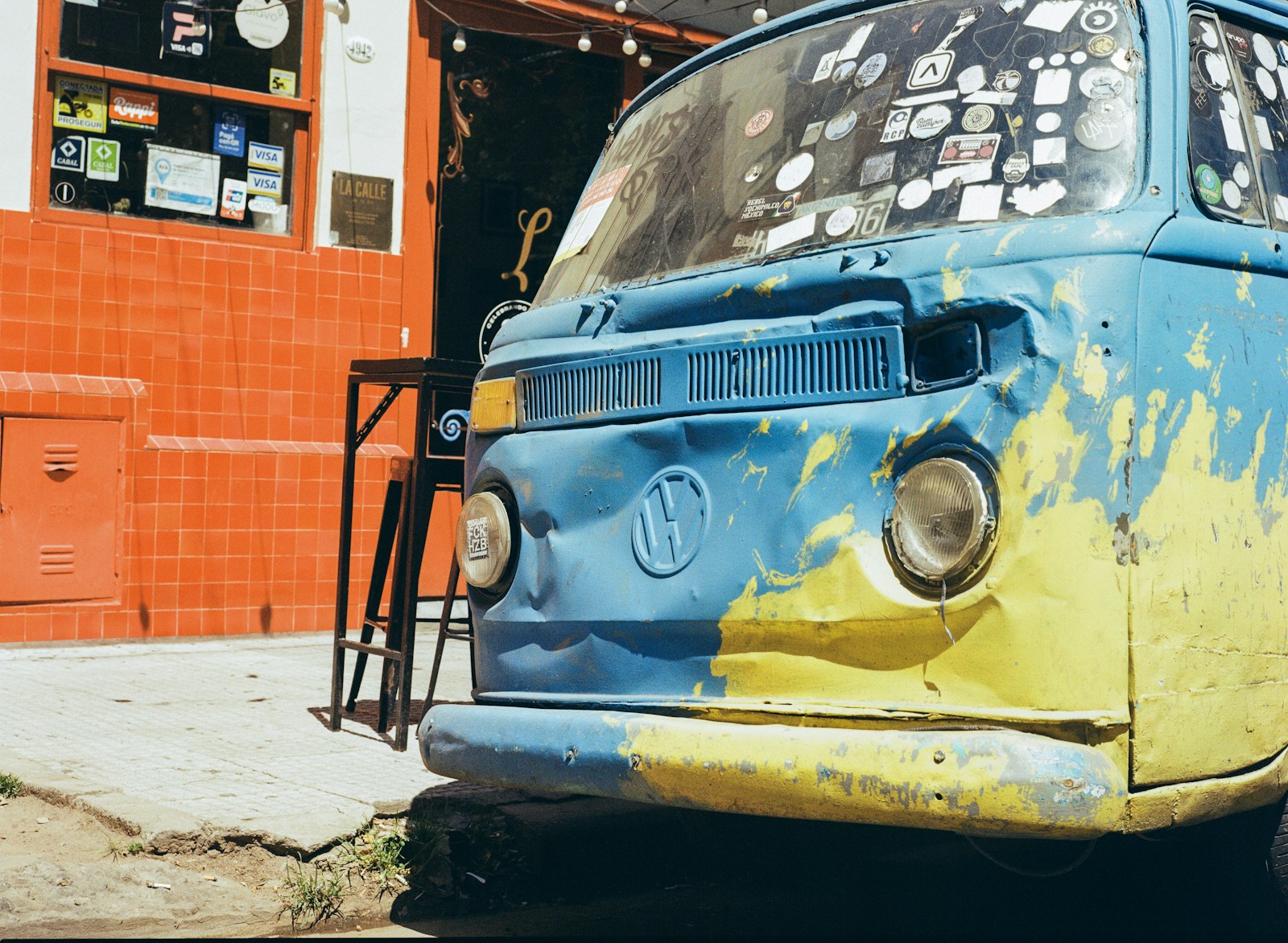 A distressed blue and yellow volkswagen van parked outside.